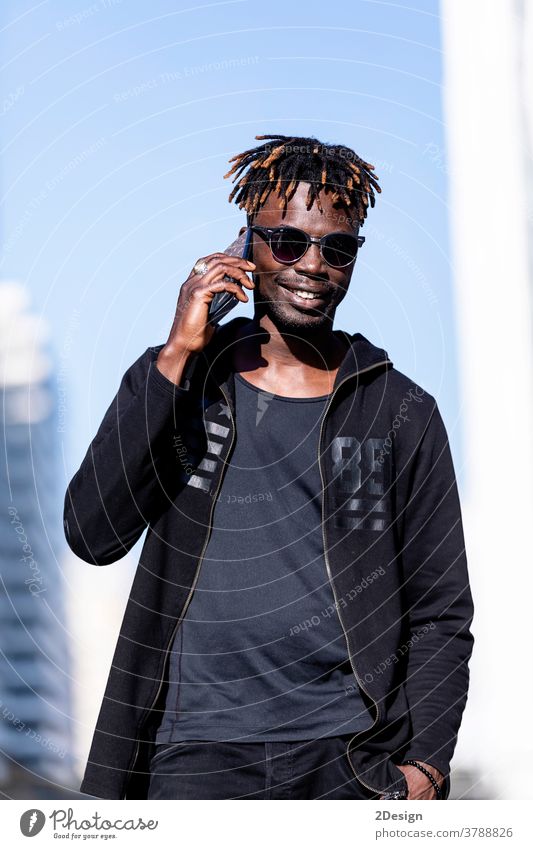 Schwarzer lächelnder Mann mit Sonnenbrille, der im Freien ein Mobiltelefon benutzt Afrikanisch schwarz Lächeln Menschen männlich Erwachsener Handy Typ Lifestyle