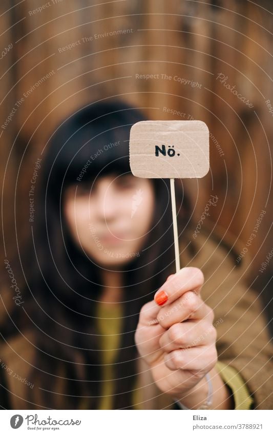 Eine dunkelhaarige Frau hält ein Schild mit der Aufschrift Nö hoch. Ablehnung, nein sagen, Trotz. Nein Protest Kommunizieren Absage nein heißt nein Weigerung