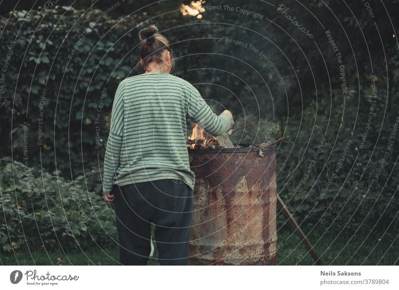 Verbrennen alter Zweige Lauf Frau Mensch Erwachsene brennend Feuer Farbfoto Licht Außenaufnahme Wärme Metallfass Garten Bäume Buchse Natur Brandwunde