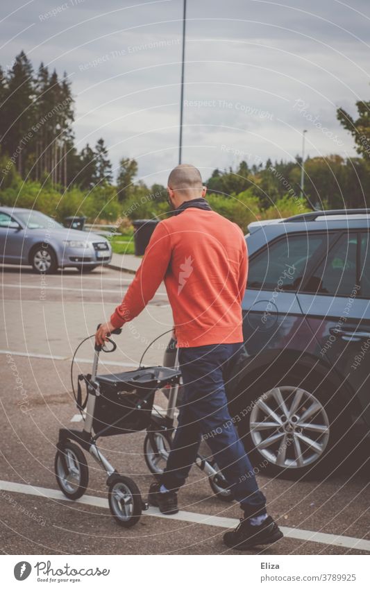 Ein junger Mann schiebt einen Rollator auf einem Parkplatz zum Kofferraum eines Autod Gehhilfe Pfleger Assistent Behindertenbetreuung Mobilität Hilfe