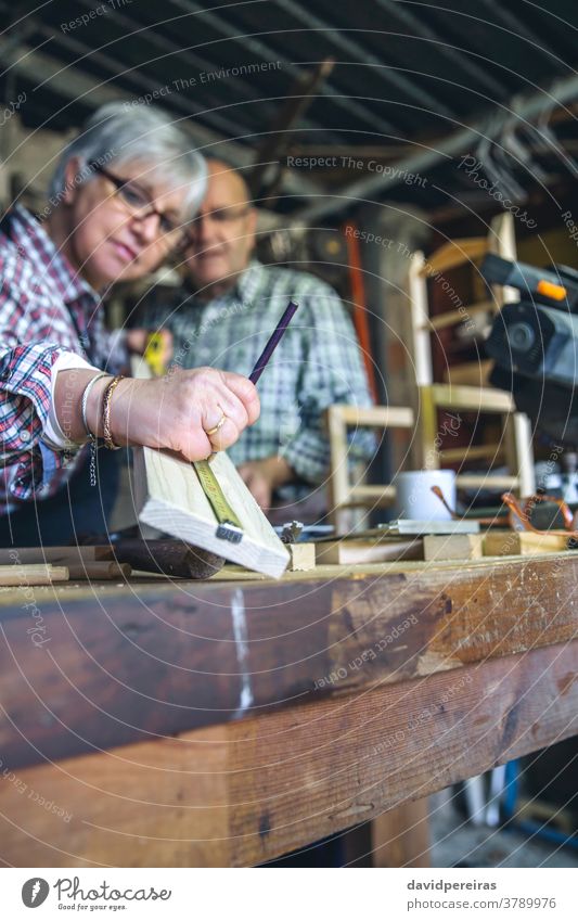 Seniorenpaar in einer Tischlerei Schreinerei Frau Messung Meter Mark Schiffsplanken Holzlatte Werkstatt Zusammensein zusammenarbeiten Hilfe Hobby Zimmerer Beruf