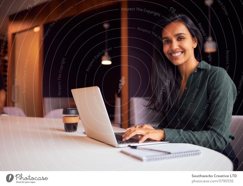 Porträt einer Geschäftsfrau, die am Besprechungstisch sitzt und am Laptop in einem modernen Großraumbüro arbeitet Business Geschäftsfrauen Sitzung Büro Sitzen
