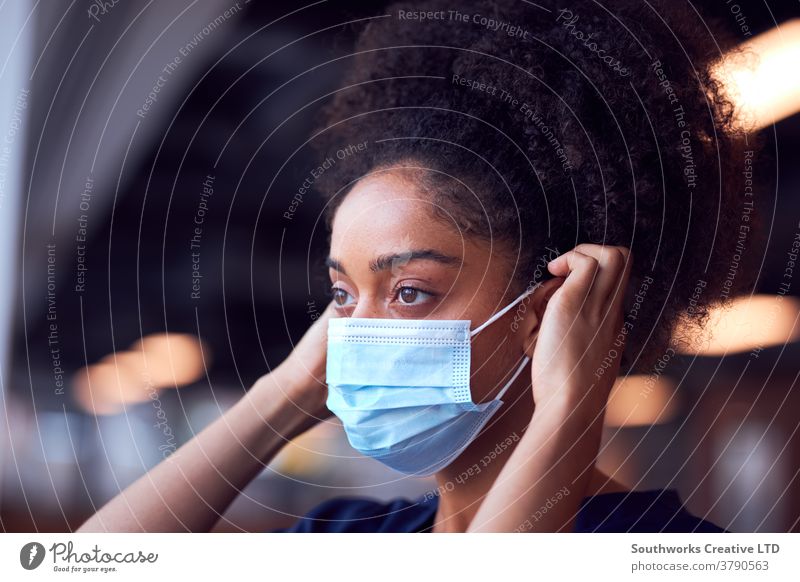 Ärztin in OP-Kleidung setzt während einer Gesundheitspandemie Gesichtsmaske unter Druck im geschäftigen Krankenhaus auf Arzt Krankenpfleger bürstet