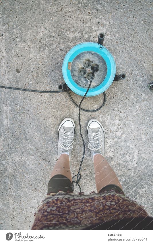 kabeltrommel mit stromanschluss auf asphalt, daneben die beine einer weiblichen person Kabeltrommel Stromanschluss portabel Stromstecker Stromkabel Anschluss