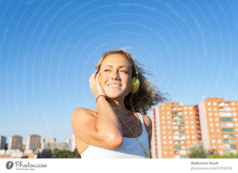 Positive Frau im Sport-BH hört Musik über Kopfhörer positiv optimistisch zuhören genießen Klang unterhalten Apparatur heiter sonnig Sommer jung Melodie Gesang