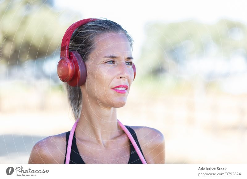Fröhliche Sportlerin mit Kopfhörer im Park stehend positiv zuhören Fitness Gerät passen Inhalt aktiv Training Musik schlank Vitalität Athlet Aktivität sportlich