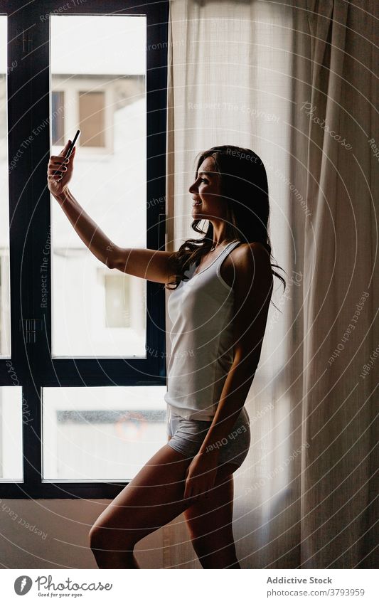Fröhliche Frau in Schlafanzug nehmen Selfie zu Hause Morgen heimwärts Fenster Nachtwäsche heiter Smartphone Glück Schlafzimmer teilen jung Teenager