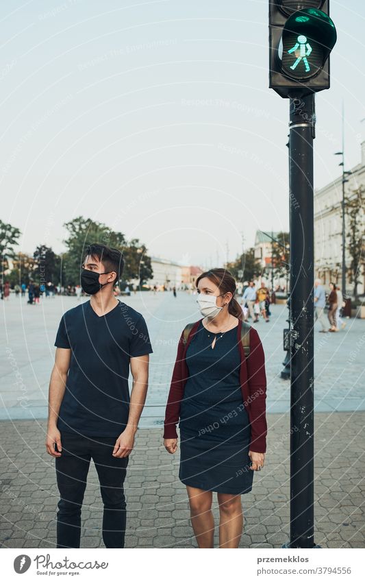 Mann und Frau, die am Fußgängerüberweg neben der Ampel warten und die Gesichtsmasken tragen, um eine Virusinfektion zu vermeiden und die Ausbreitung der Krankheit im Falle eines Coronavirus zu verhindern