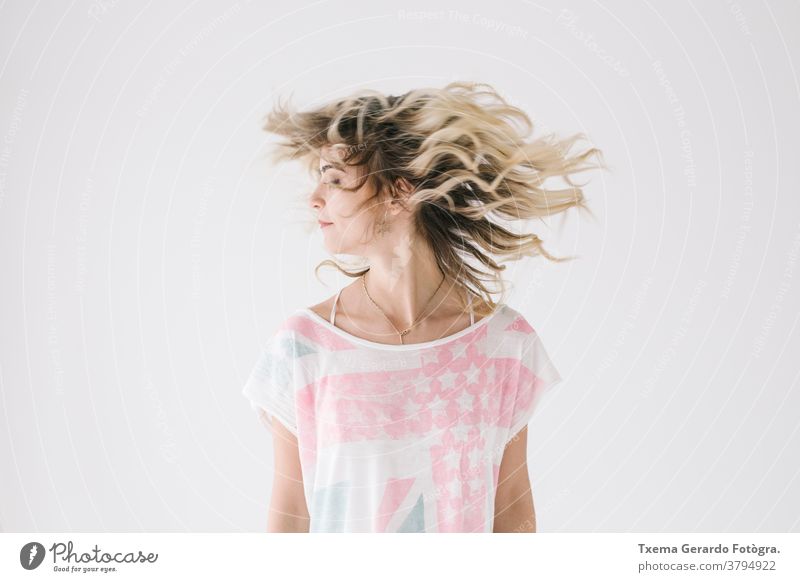 Natürliches Porträt eines blonden Mädchens, das sein Haar schüttelt, auf weißem Hintergrund natürlich Behaarung Bewegung schütteln Hemd ungefiltert Ausdruck