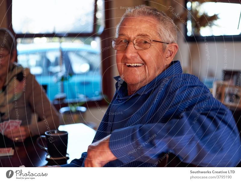 Porträt eines lächelnden älteren Paares, das zu Hause am Tisch sitzt und gemeinsam Karten spielt Senior Senioren in den Ruhestand getreten Spielen Kartenspiel