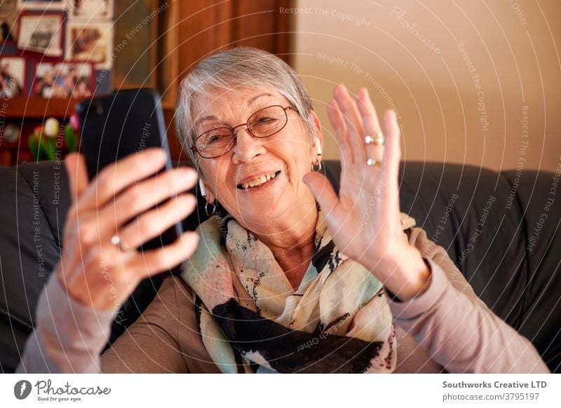 Lächelnde ältere Frau zu Hause winkt, während sie einen Videoanruf an die Familie auf dem Mobiltelefon tätigt Senior Video-Chat Mobile Senioren Zelle Handy