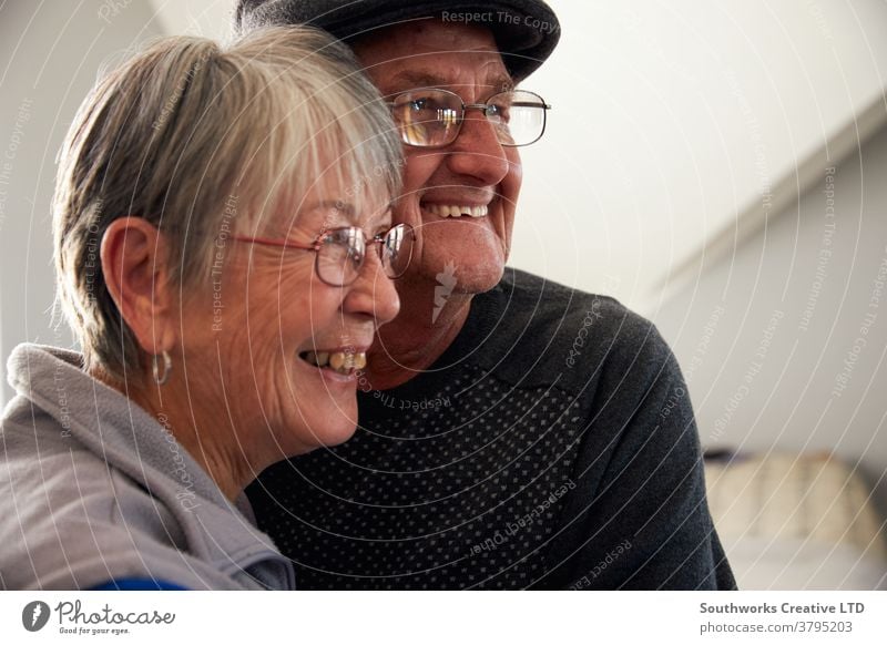 Liebende ältere Paare, die lachen und lächeln, während sie sich zu Hause umarmen Senior Senioren in den Ruhestand getreten entspannend Stehen Fenster liebevoll