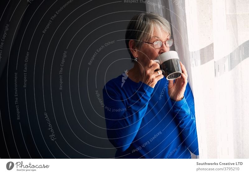 Ältere Frau entspannt am Fenster stehend zu Hause mit heißem Getränk Senior Senioren in den Ruhestand getreten entspannend Stehen trinken Heißgetränk Tasse Tee