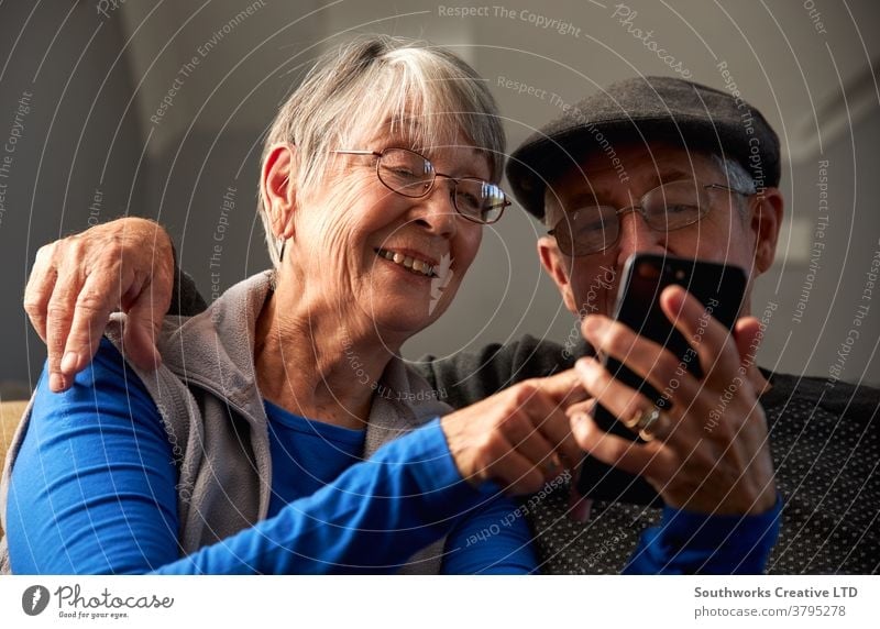 Älteres Ehepaar zu Hause auf dem Sofa sitzend und gemeinsam mobil telefonierend Paar Senior Senioren Mobile Handy Zelle verbunden online Technologie