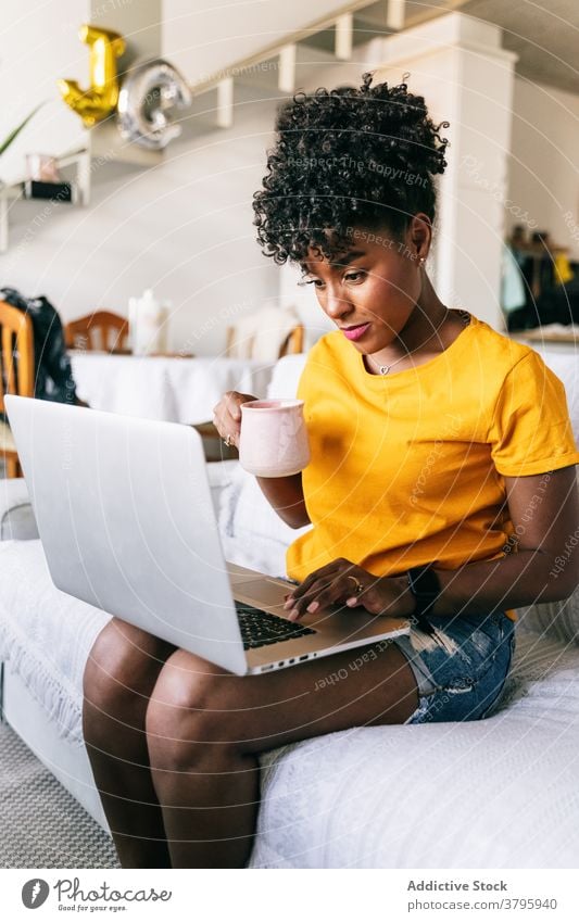 Junge schwarze Frau trinkt Kaffee und verwendet Laptop zu Hause heimwärts benutzend trinken Browsen freiberuflich abgelegen online jung Afroamerikaner ethnisch
