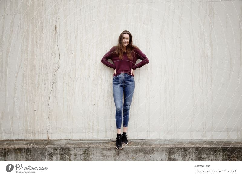 Portrait einer jungen Frau die vor einer Betonwand auf einer Mauer steht junge Frau 18-25 Jahre warmherzig schön charmant schlank brünett lange Haare frisch