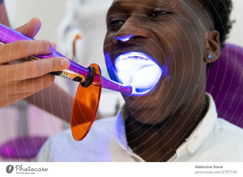 Crop-Arzt mit Dentallicht während des Eingriffs dental Kur Licht Zahnarzt geduldig Stomatologie uv ultraviolett Leckerbissen Verfahren ethnisch schwarz