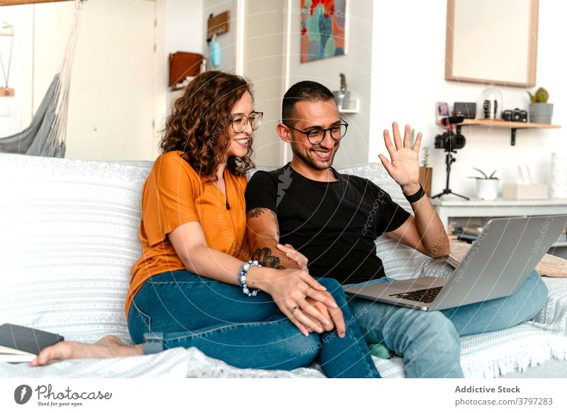 Glückliches Paar mit Video-Gespräch auf Laptop zu Hause Videoanruf Zusammensein Händchenhalten Sofa heimwärts Wellenhand heiter Anschluss Partnerschaft Freund