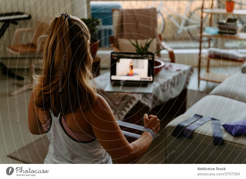 Unerkennbare Sportlerin trainiert mit Gummiband zu Hause Übung Widerstandsband Tutorial Training Vitalität Energie üben online Laptop zuschauen folgen Gerät