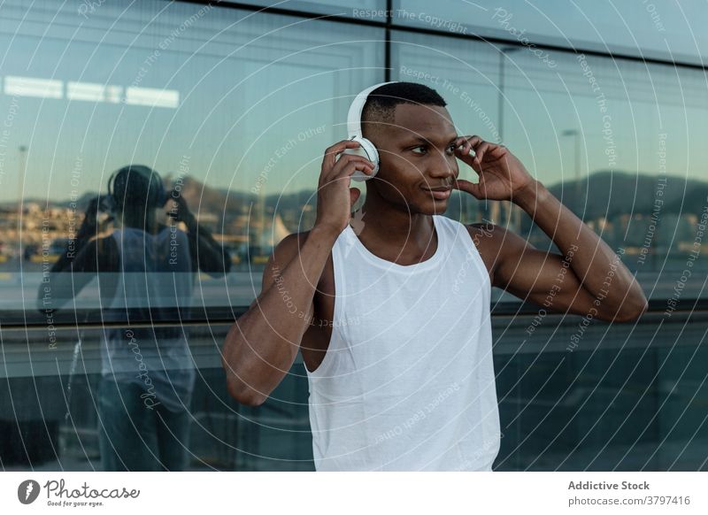 Fröhlicher schwarzer Mann, der mit Kopfhörern Musik hört heiter zuhören Freude Klang Athlet Drahtlos Optimist männlich Training Gerät Apparatur Lächeln Melodie