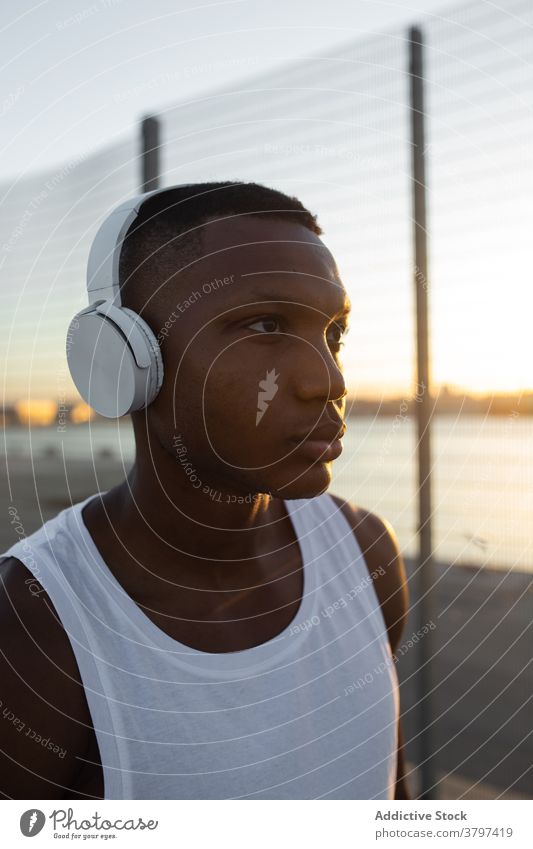 Schwarzer Sportler mit Kopfhörern beim Ausruhen nach dem Training Mann Athlet ernst muskulös sportlich Musik zuhören passen männlich Sportbekleidung Lifestyle