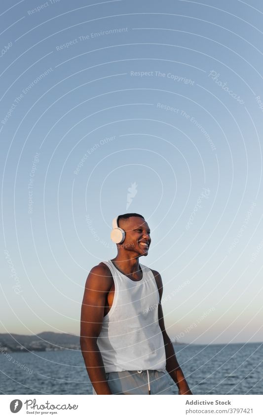 Schlanker schwarzer Mann an der Strandpromenade beim Training Läufer Lächeln Aufwärmen Kopfhörer Dehnung Energie Glück Konzentration Wohlbefinden männlich