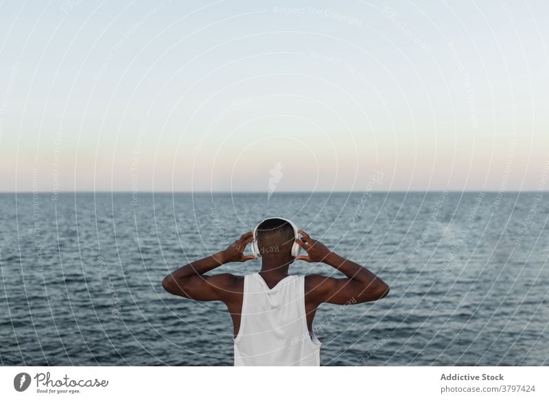 Schlanker schwarzer Mann, der sich beim Training an der Strandpromenade dehnt Läufer Hafengebiet Aufwärmen Kopfhörer Dehnung Energie Konzentration Wohlbefinden