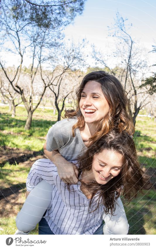 zwei Mädchen einen Park von Mandelbäumen, die zusammen lachend aufeinander kletterten Aktivität Hintergrund schön hell nachlässig heiter farbenfroh Frau Freunde