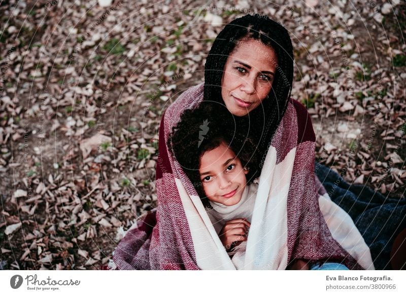 Porträt einer hispanischen Mutter und eines Afrokindermädchens, die sich draußen in der Natur entspannen. Herbstsaison. Konzept Familie Tochter im Freien