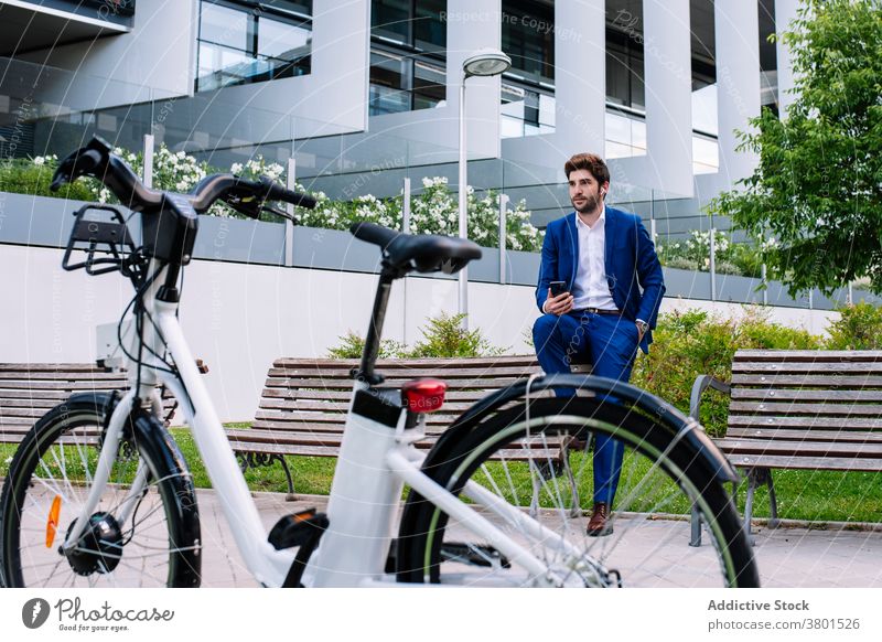 Stilvoller Unternehmer im formalen Anzug schaut auf Armbanduhr auf Bank Geschäftsmann stylisch elektrisch Fahrrad Stadt maskulin gutaussehend Gerät Großstadt