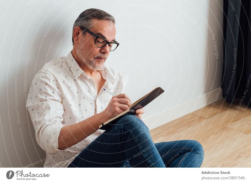 Konzentrierter Mann macht sich Notizen in einem Notizbuch, während er auf dem Boden sitzt schreiben zur Kenntnis nehmen Hinweis Notebook ernst Fokus
