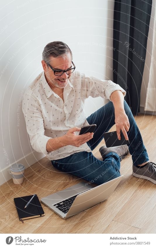 Positiv reifen Mann mit Smartphone und Laptop auf dem Boden Arbeitsbereich benutzend Browsen Fokus positiv Apparatur Gerät zuschauend klug Konzentration Stock