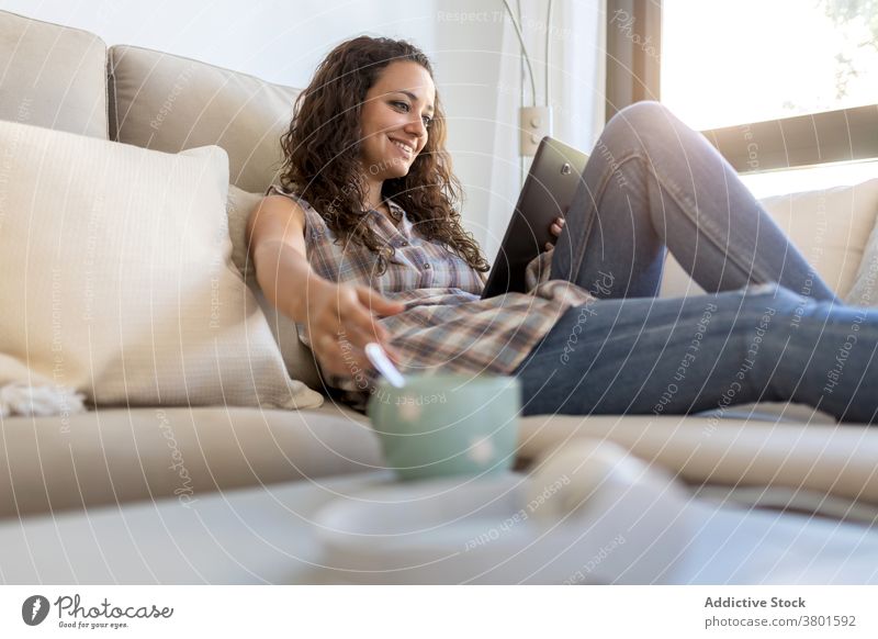 Fröhliche Frau, die im Wohnzimmer auf einem Tablet surft Browsen Tablette sich[Akk] entspannen heimwärts unterhalten benutzend Nachricht heimisch Wochenende