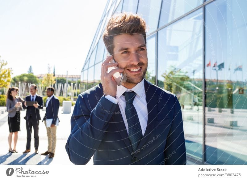 Glücklicher junger Geschäftsmann spricht auf Smartphone auf der Straße Mann reden Gespräch Kommunizieren stilvoll selbstbewusst Unternehmer Anruf Gebäude