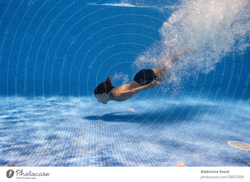 Teenager-Junge taucht ins Poolwasser Energie Sinkflug schwimmen aktiv unter Wasser Aktivität sorgenfrei spielerisch platschen aqua Resort Eintauchen genießen