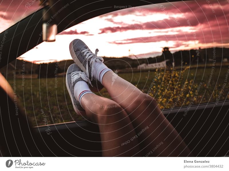 junge Frau mit Turnschuhen, deren Füße bei Sonnenuntergang auf das Autofenster gestützt werden Beine Reise Menschen Lifestyle Sonnenlicht Straße PKW Ausflug