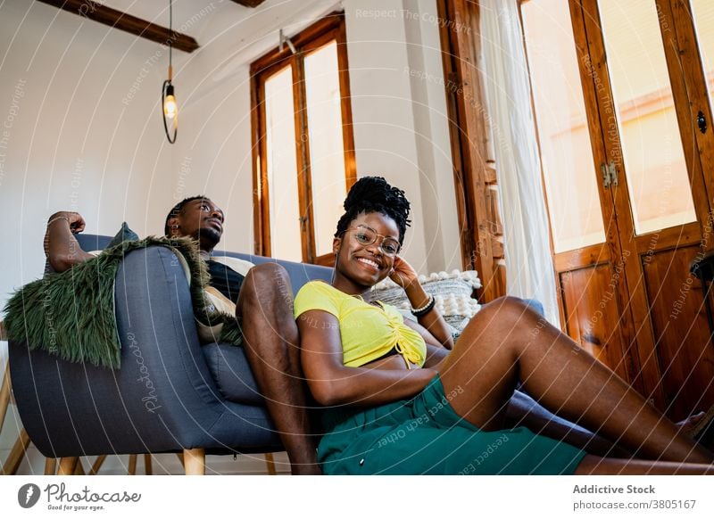 Schwarzes Paar entspannt im Wohnzimmer heiter ruhen Sofa gemütlich Innenbereich Freizeit Wochenende Kälte Afroamerikaner schwarz Teppich Tisch Rahmen hölzern