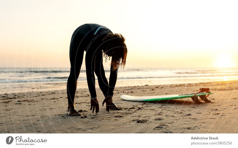Unkenntlich schwarz Surfer Stretching an der Küste des Ozeans Mann Dehnung Surfbrett MEER Meer Pause Wassersport Skimboard Strand männlich krause Haare ethnisch
