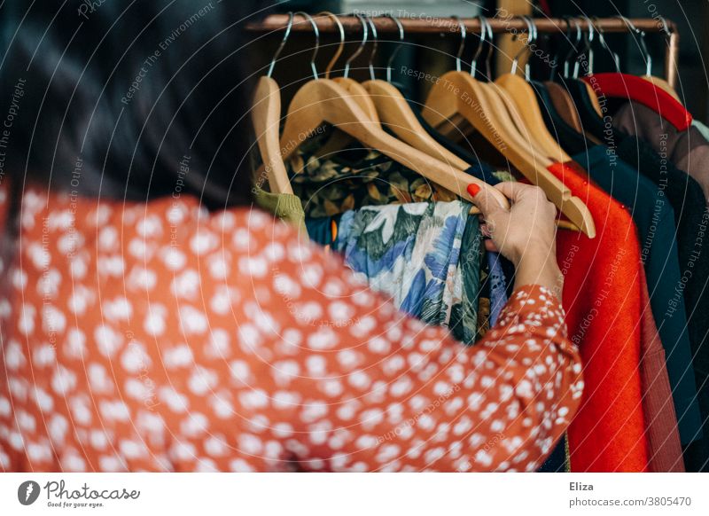 Eine Frau stöbert nach Kleidung an einer Kleiderstande im Second Hand Geschäft oder Flohmarkt Kleiderstange vintage shoppen stöbern nachhaltig Mode Klamotten