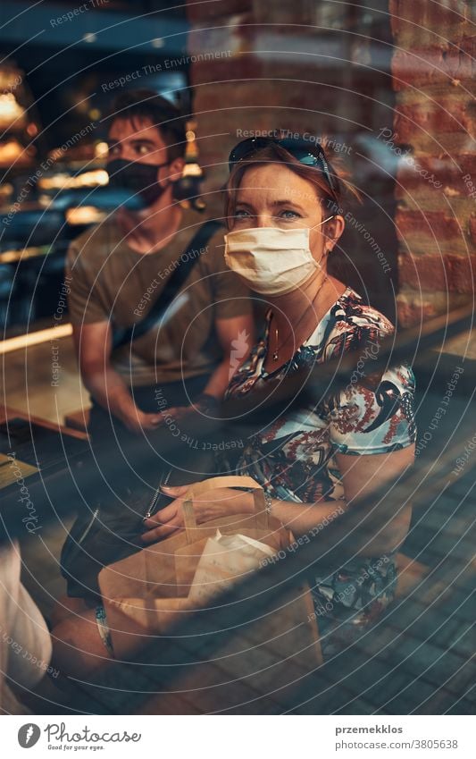 Familie sitzt im Café an der Ladenfront im Stadtzentrum und trägt die Gesichtsmaske, um eine Virusinfektion zu vermeiden Kaukasier Gespräch covid-19 Lifestyle