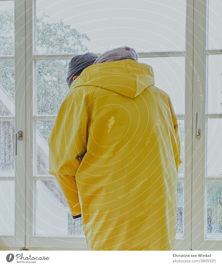 Mann steht bei Regenwetter am Fenster und zieht einen Friesennerz an | gefangen in Plastik Regenjacke Regenmantel schlechtes Wetter Schietwetter gelb