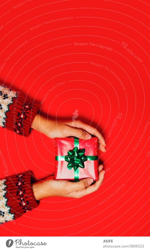 Frauenhände mit einem Winterpullover, der ein Weihnachtsgeschenk auf rotem Hintergrund hält. Weihnachten Geschenk Kasten präsentieren Hände Geben Entgegennahme