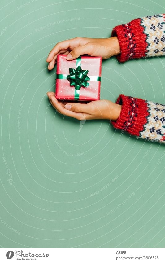 Frauenhände mit einem Winterpullover, der ein Weihnachtsgeschenk auf grünem Hintergrund hält. Weihnachten Geschenk Kasten präsentieren Hände Geben Entgegennahme