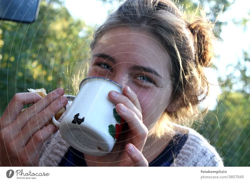 junge Frau im Grünen trinkt lächelnd aus einem Emaille-Becher trinken Emailletasse Tasse Frühstück Camping Heißgetränk Kaffee Getränk Kaffeepause Kaffeetasse
