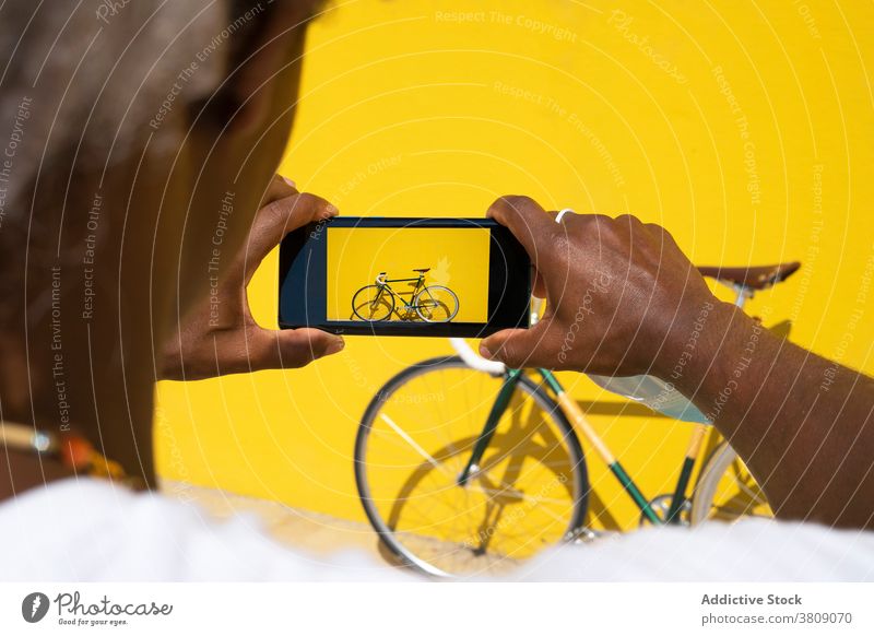 Schwarzer Mann nimmt ein Foto von seinem Fahrrad mit dem Telefon auf einem gelben fotografierend Mobile Online-Verkauf ein Fahrrad verkaufen