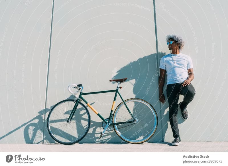Schwarzer Radfahrer, der neben seinem Stadtrad an einer grauen Wand lehnt. schwarzer Radfahrer Reiter Schwarzer Reiter Fahrrad Afro-Look Schwarzer Mann