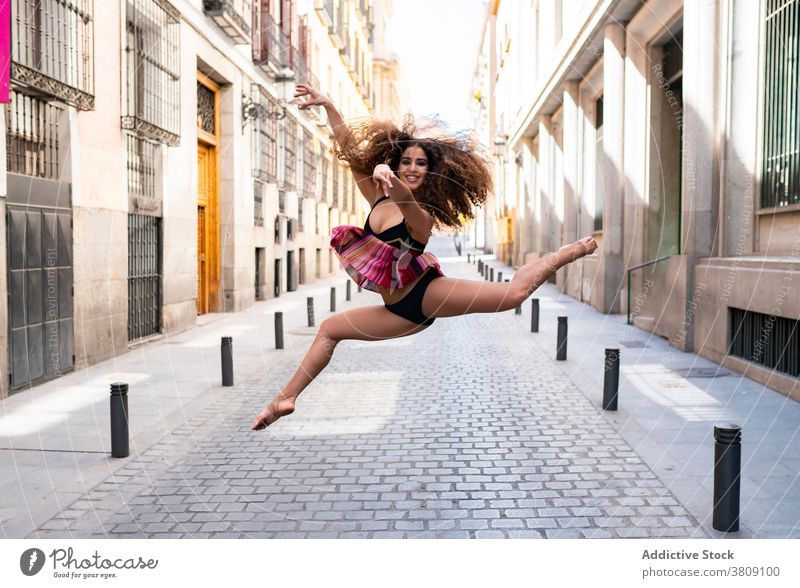 Fröhliche junge ethnische Ballerina springt auf der Straße Frau springen Glück Tanzen ausführen Balletttänzer Lächeln beweglich Energie Bewegung Tänzer passen