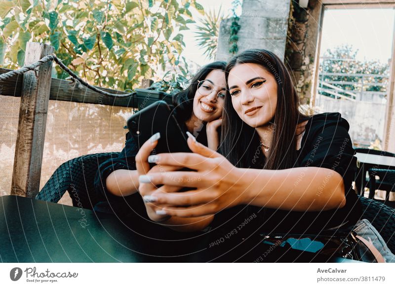 Ein Paar junge Frauen, die lächelnd in einer Bar ein Selfie machen Foto Telefon Glück brünett Freunde freudig Dame tausendjährig außerhalb Lächeln stylisch