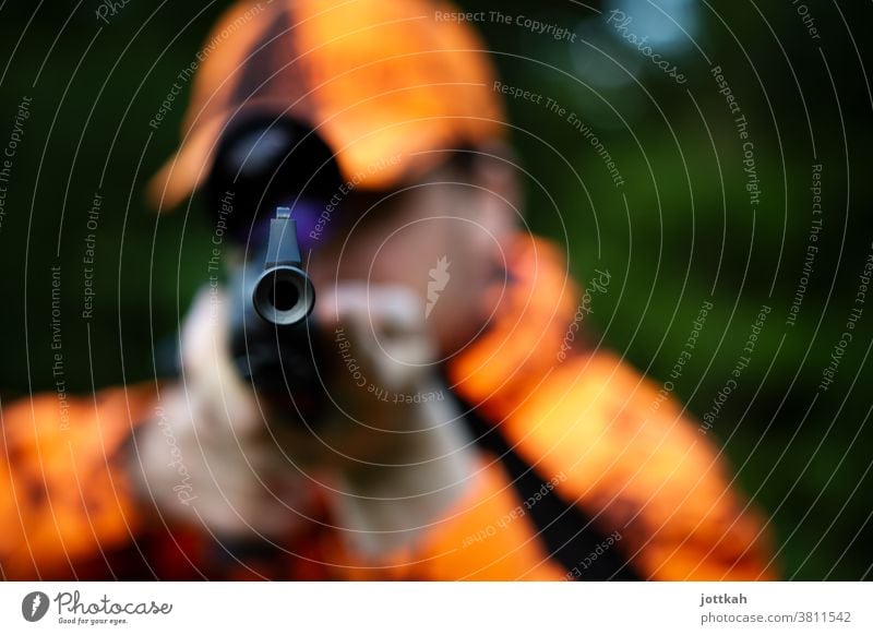 Blick in den Lauf eines Jagdgewehrs, das von einem orange gekleideten Jäger gehalten wird. Der Fokus liegt auf der Mündung der Waffe. Gewehr Flinte Schusswaffe