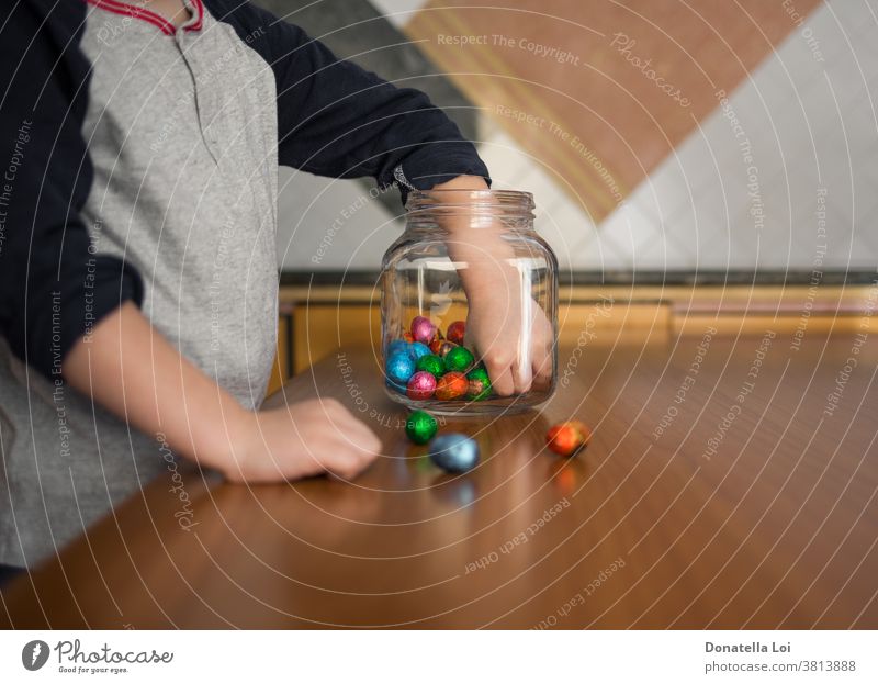 Kind nimmt Pralinen aus der Dose zu Hause Feier Kindheit Schokolade farbig Konzept Verlangen Ostern Eier Glasgefäß Gier gierig gierige Nahrung Hand Hände Küche